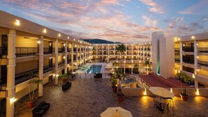 A multi-story hotel with a central courtyard featuring a swimming pool, outdoor seating, and potted plants. - Windward Passage Hotel (St. Thomas)