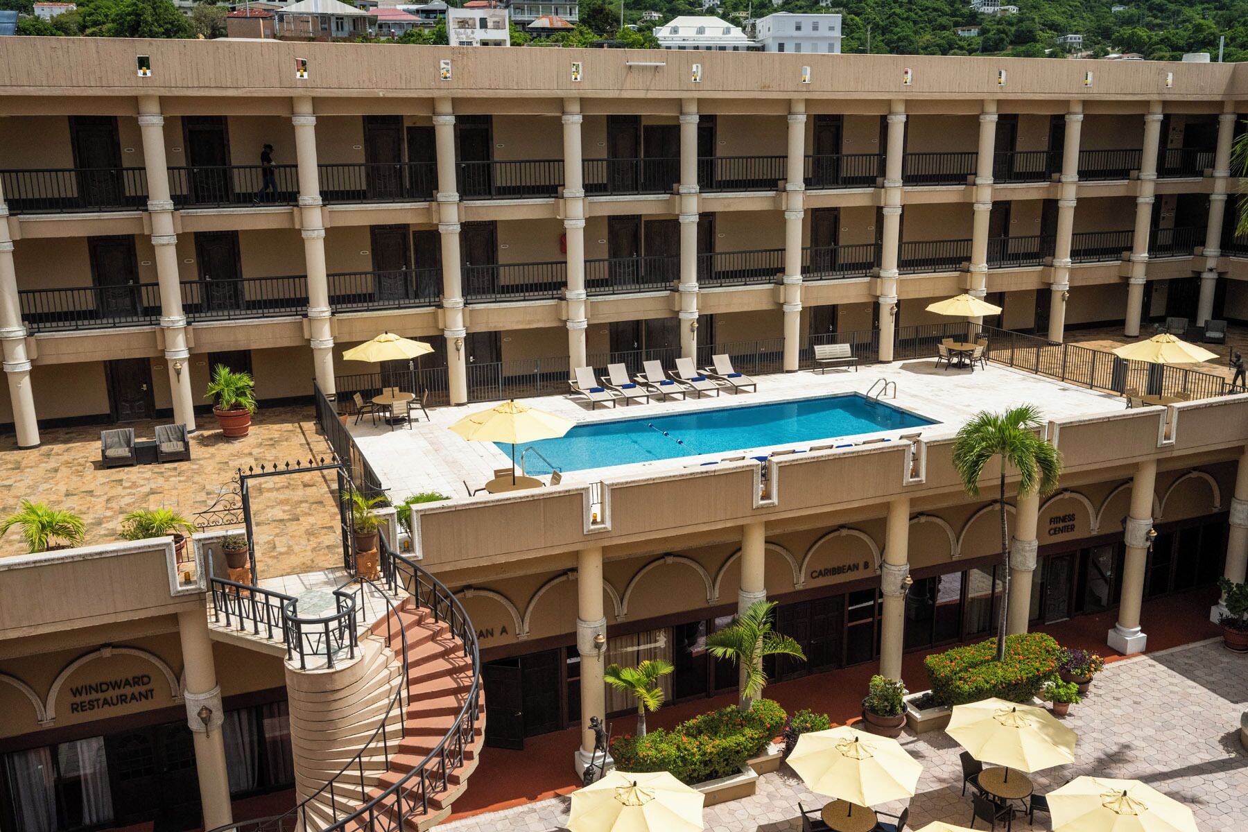 A multi-story hotel with a central courtyard featuring a swimming pool, outdoor seating, and a fitness center.