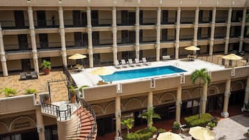 Un hotel de varios pisos con un patio central que cuenta con una piscina, mobiliario exterior y un gimnasio.