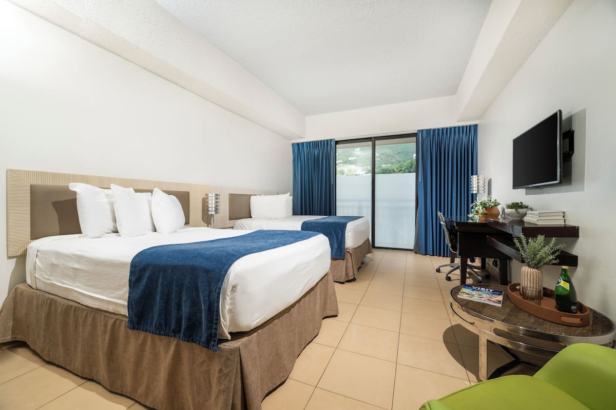 Ein Hotelzimmer mit einem großen Bett, zwei Einzelbetten, einem Schreibtisch mit Stuhl, einem Fernseher und Blick ins Freie.
