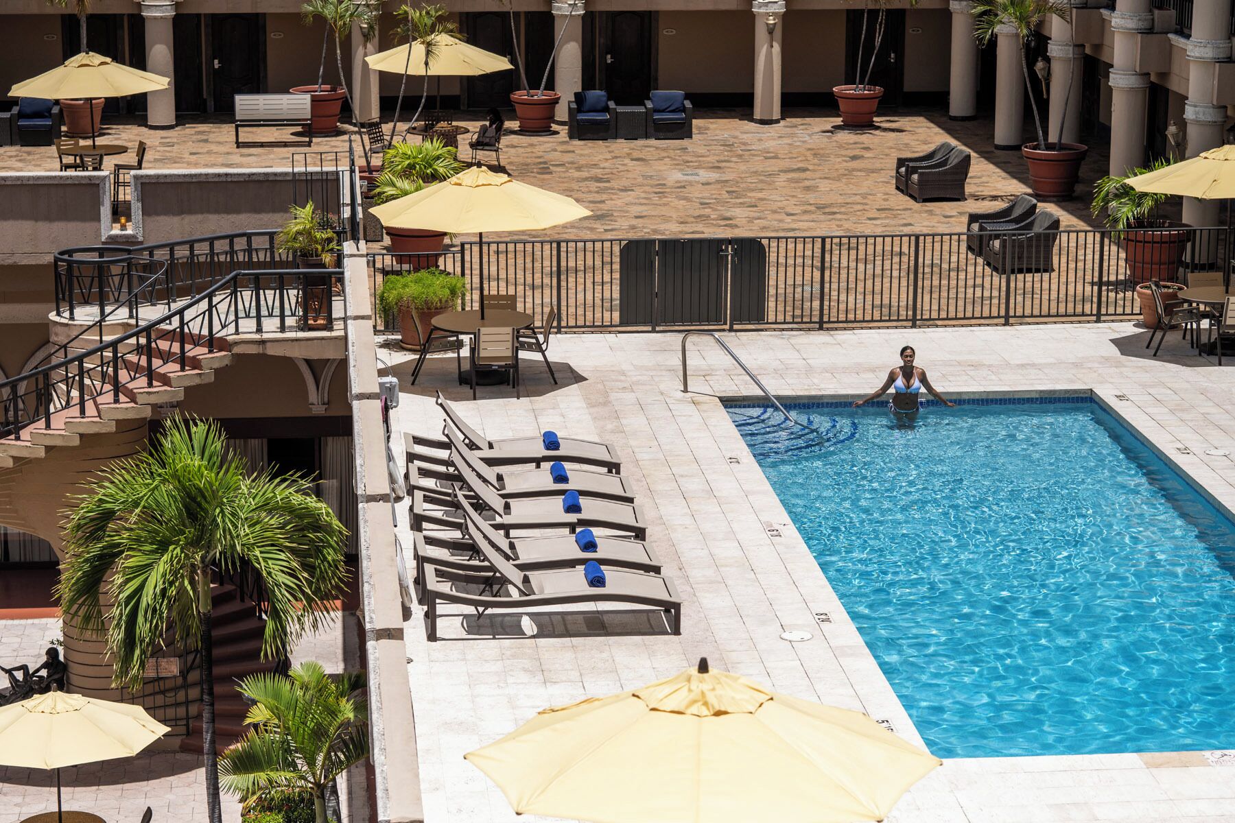 A pool area with lounge chairs, umbrellas, and a staircase leading to an upper level.