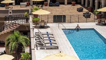 A pool area with lounge chairs, umbrellas, and a staircase leading to an upper level.