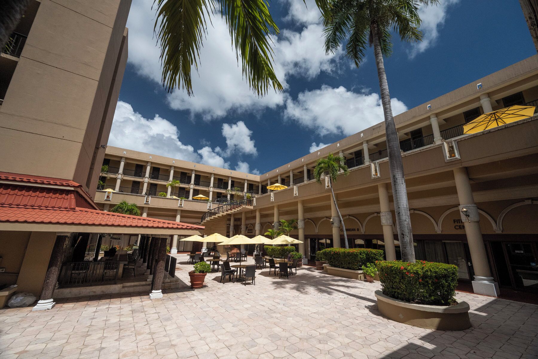 A multi-story hotel with outdoor seating areas, palm trees, and a clear sky.