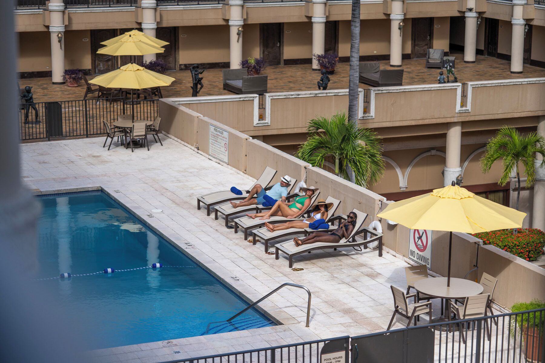 A pool area with lounge chairs and umbrellas, a pool with a no diving sign, and a building with columns in the background.