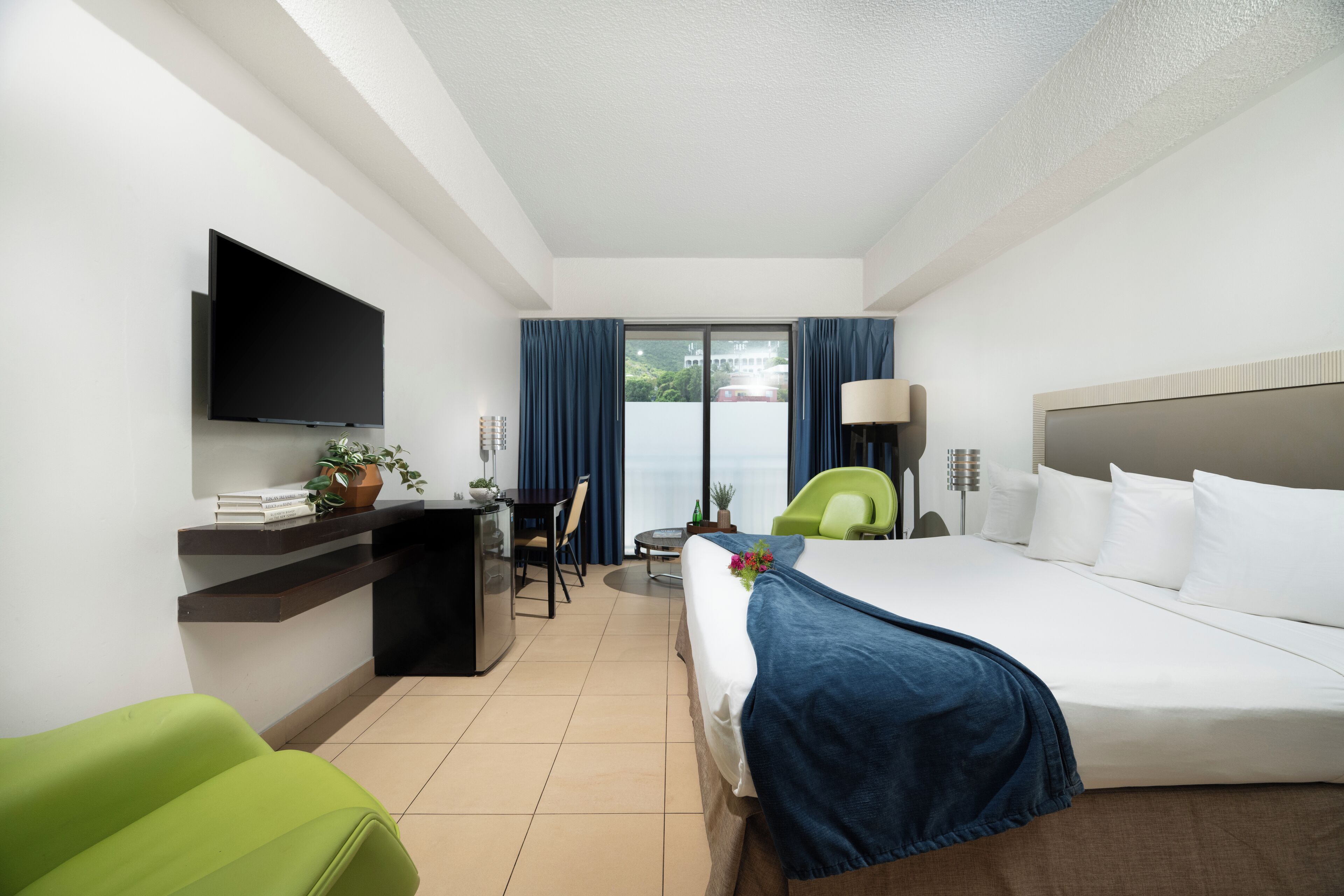 A hotel room with a bed, a desk, a chair, a TV, and a view of the outdoors.