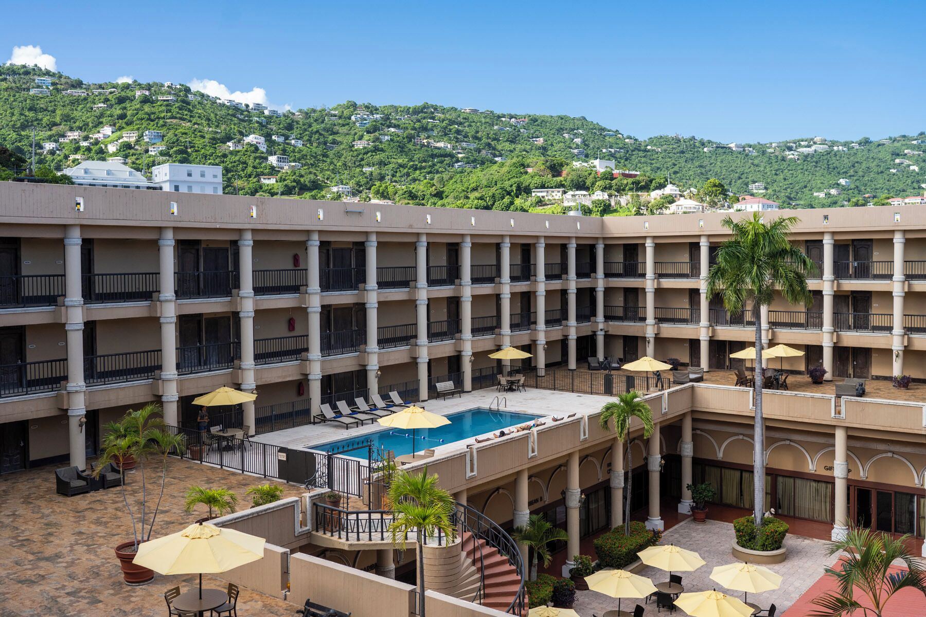 Ein Mehrstöckiges Hotel mit Innenhof, der einen Swimmingpool, Sitzgelegenheiten im Freien und Palmen umfasst.