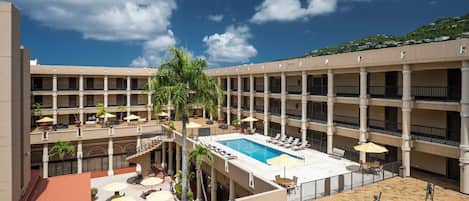 A hotel with a central pool, multiple balconies, and outdoor seating areas.