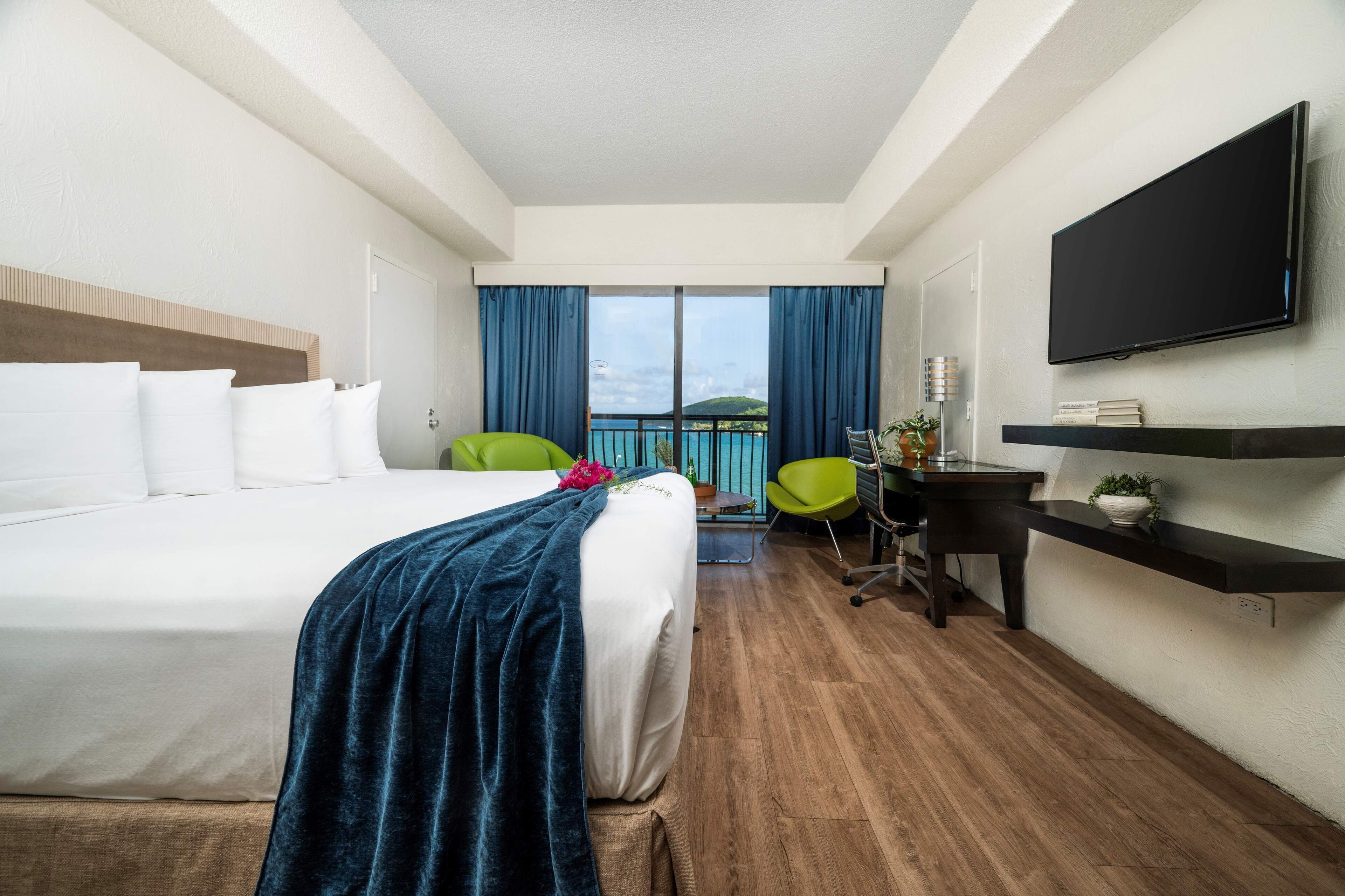 A hotel room with a bed, a desk, a chair, a TV, and a balcony with a view.