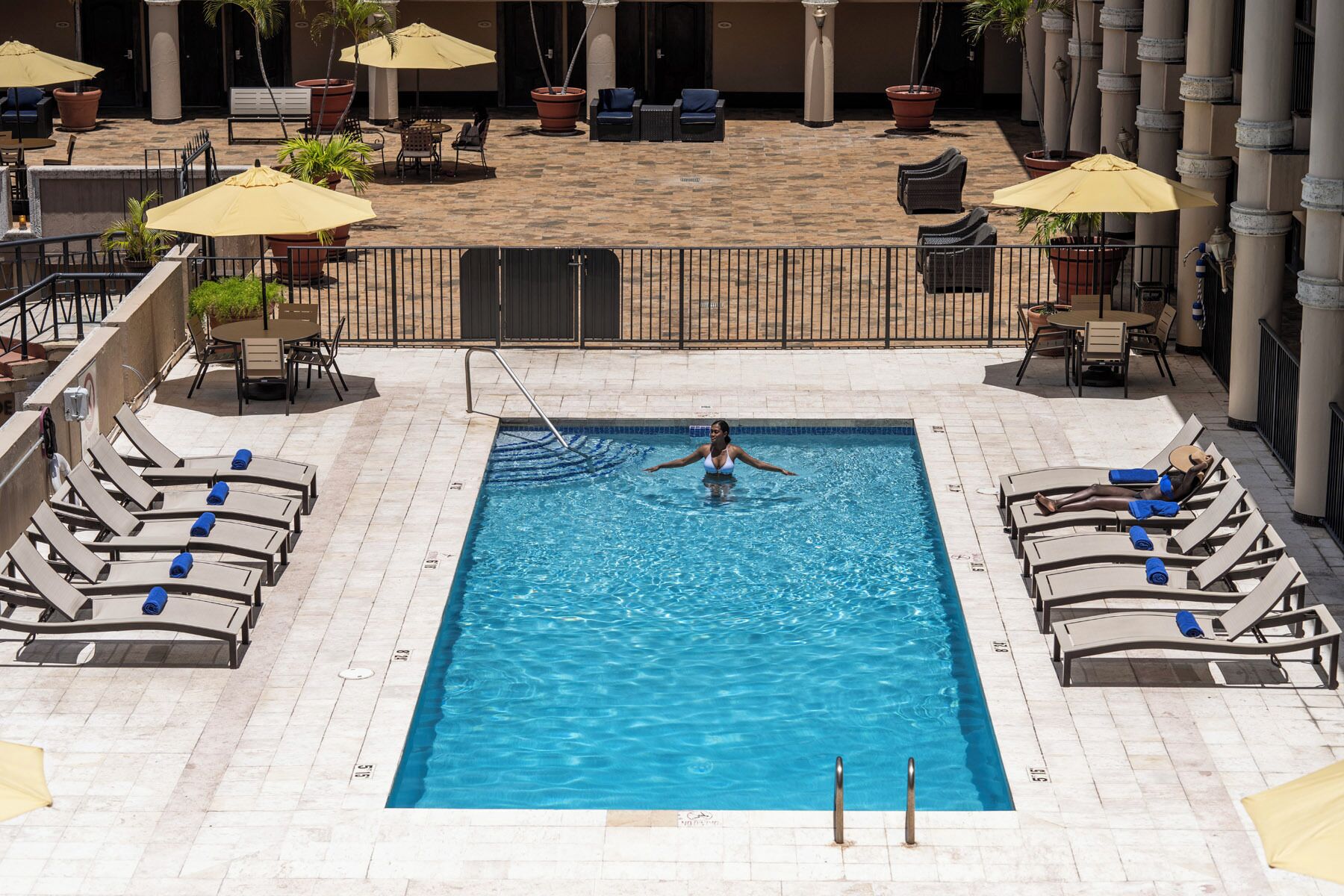 Ein Swimmingpool mit Liegestühlen und Sonnenschirmen, umgeben von einer gefliesten Terrasse.