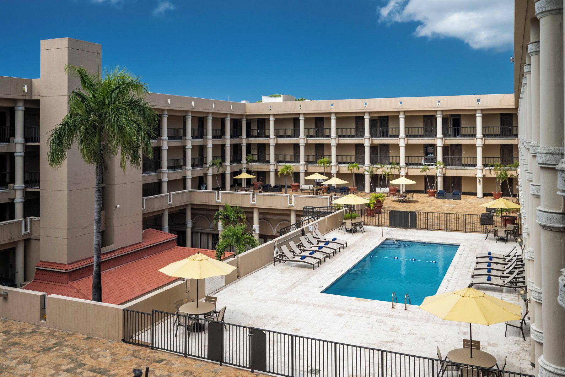 A hotel with a central pool, multiple balconies, and outdoor seating areas with umbrellas.