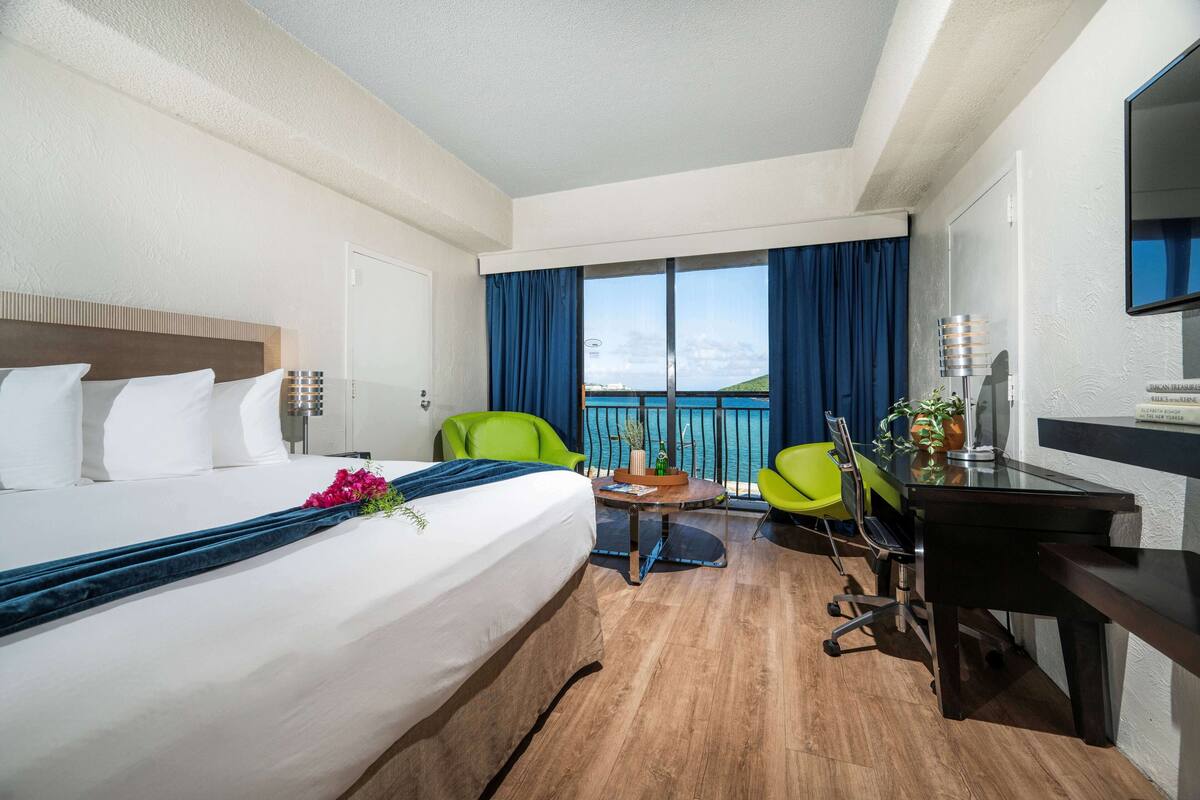 Ein Hotelzimmer mit Bett, Schreibtisch, Stuhl, einem kleinen Tisch und Blick auf den Ozean.