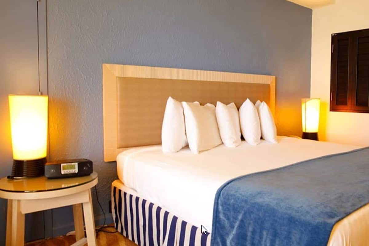 Ein Hotelzimmer mit Bett, Nachttischlampen, einem Radio und einem Fenster mit Rollläden.