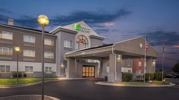 Edificio de Holiday Inn Express con una entrada bien iluminada, un área techada y una bandera estadounidense.