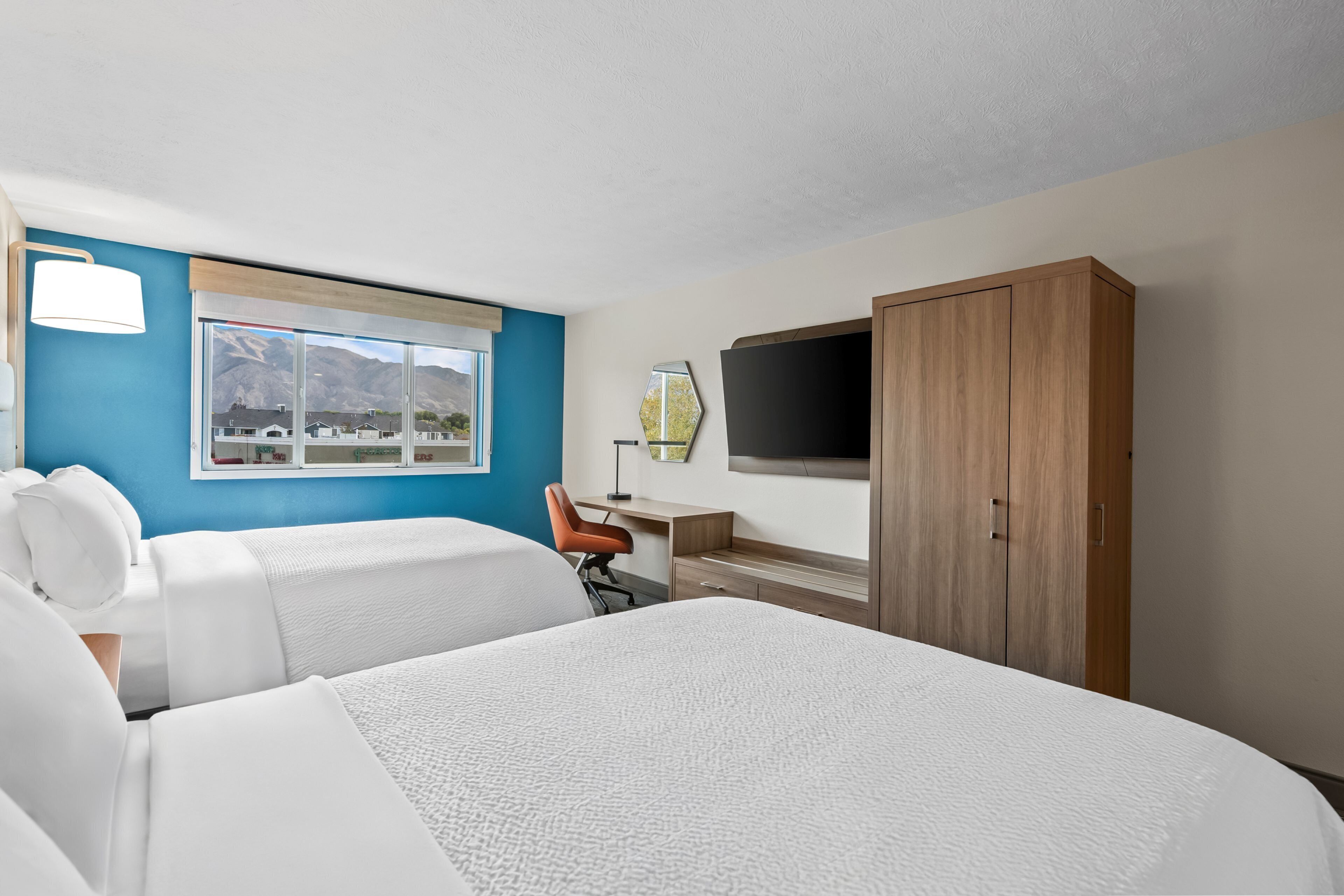 A hotel room with two beds, a desk, a chair, a TV, and a wardrobe.