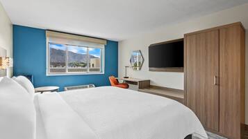 Habitación de hotel con una cama grande, un escritorio, una silla, un televisor y un armario.
