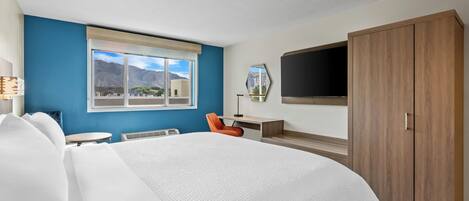 Habitación de hotel con una cama grande, un escritorio, una silla, un televisor y un armario.
