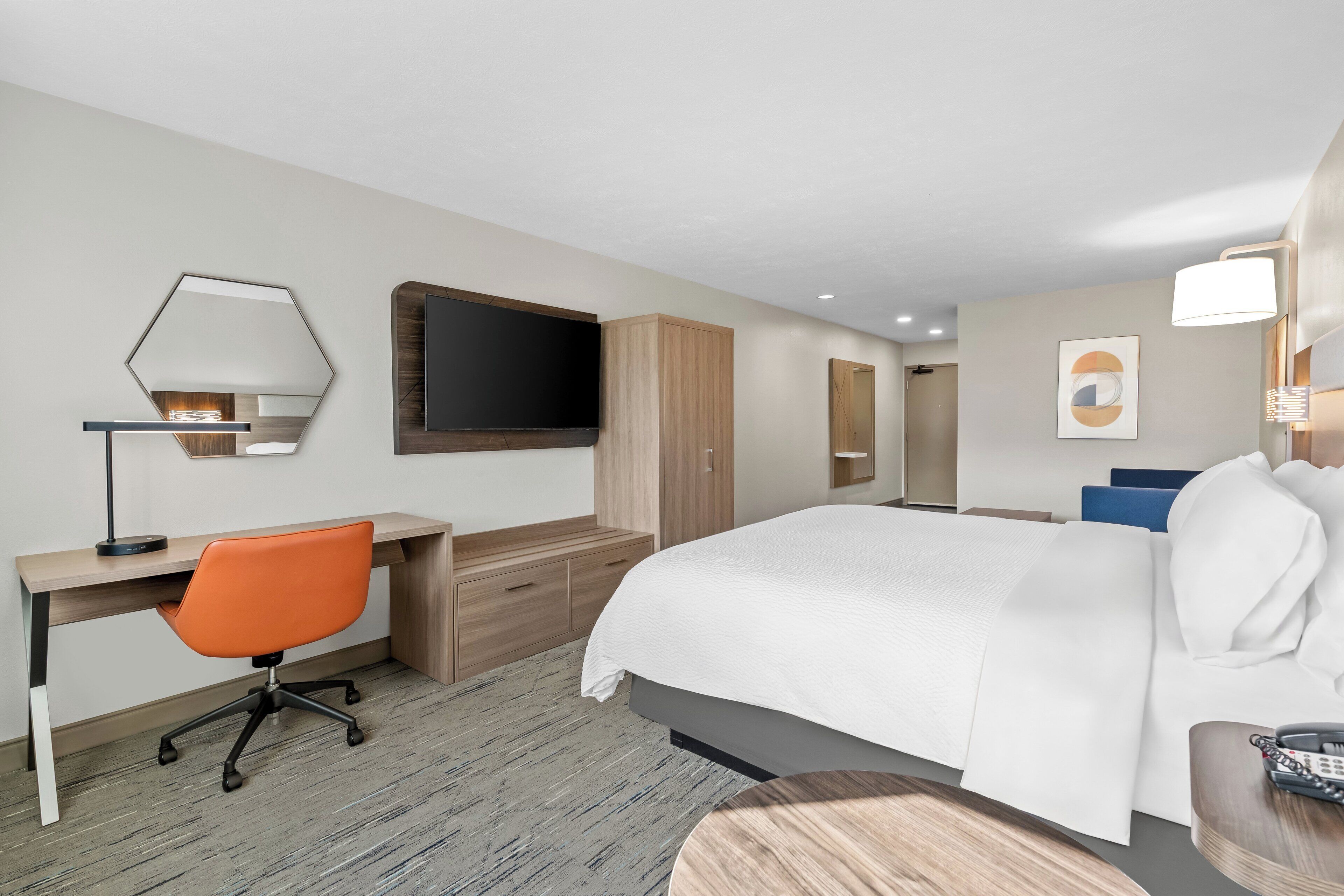 Una habitación de hotel con una cama, un escritorio con una silla naranja, un televisor y un armario.