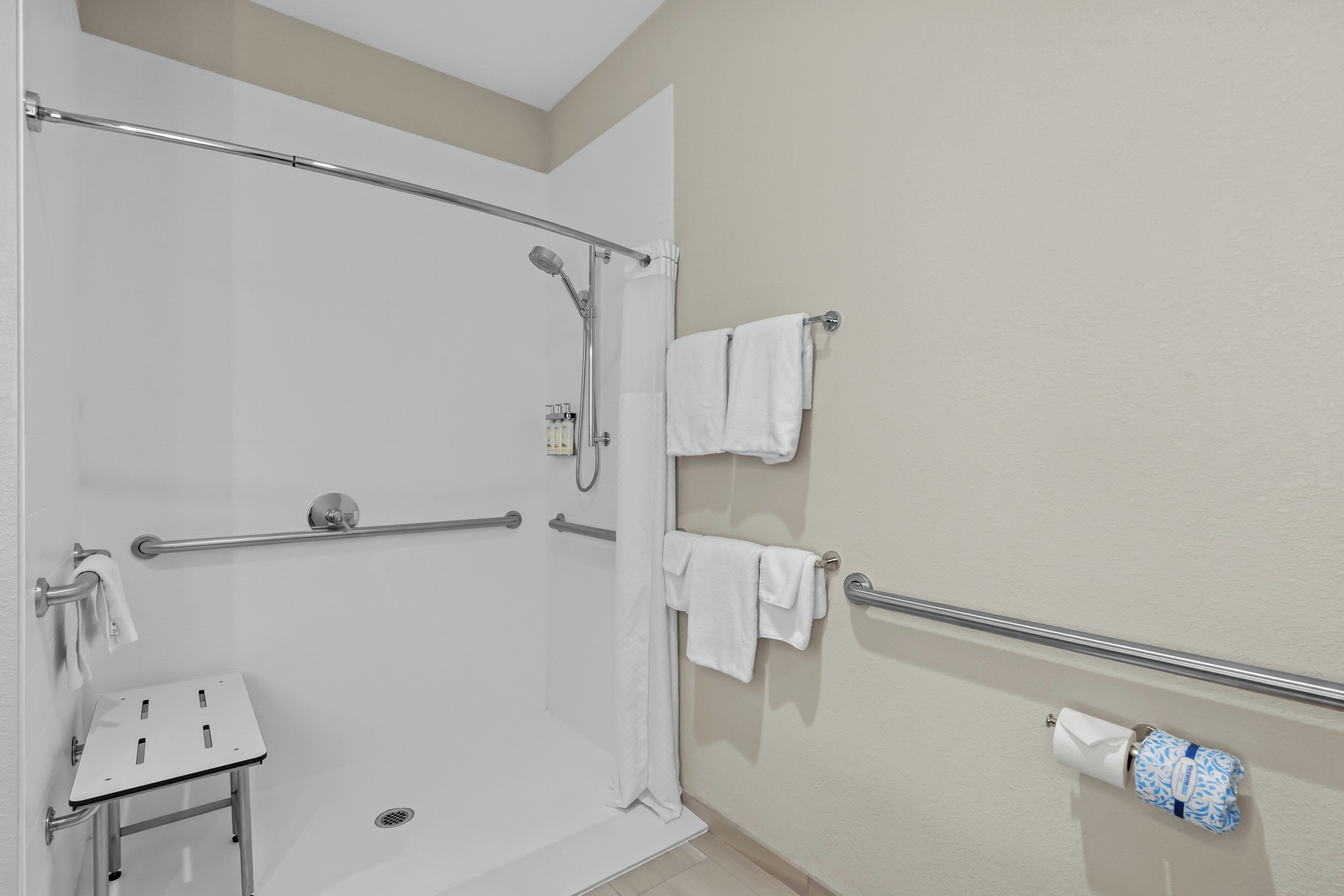 A shower area with grab bars, a small sink, and a toilet paper holder.