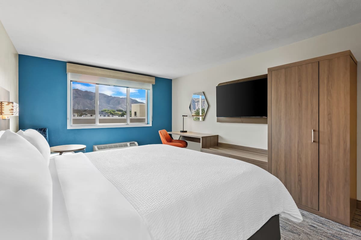 A hotel room with a large bed, a desk, a chair, a TV, and a wardrobe.