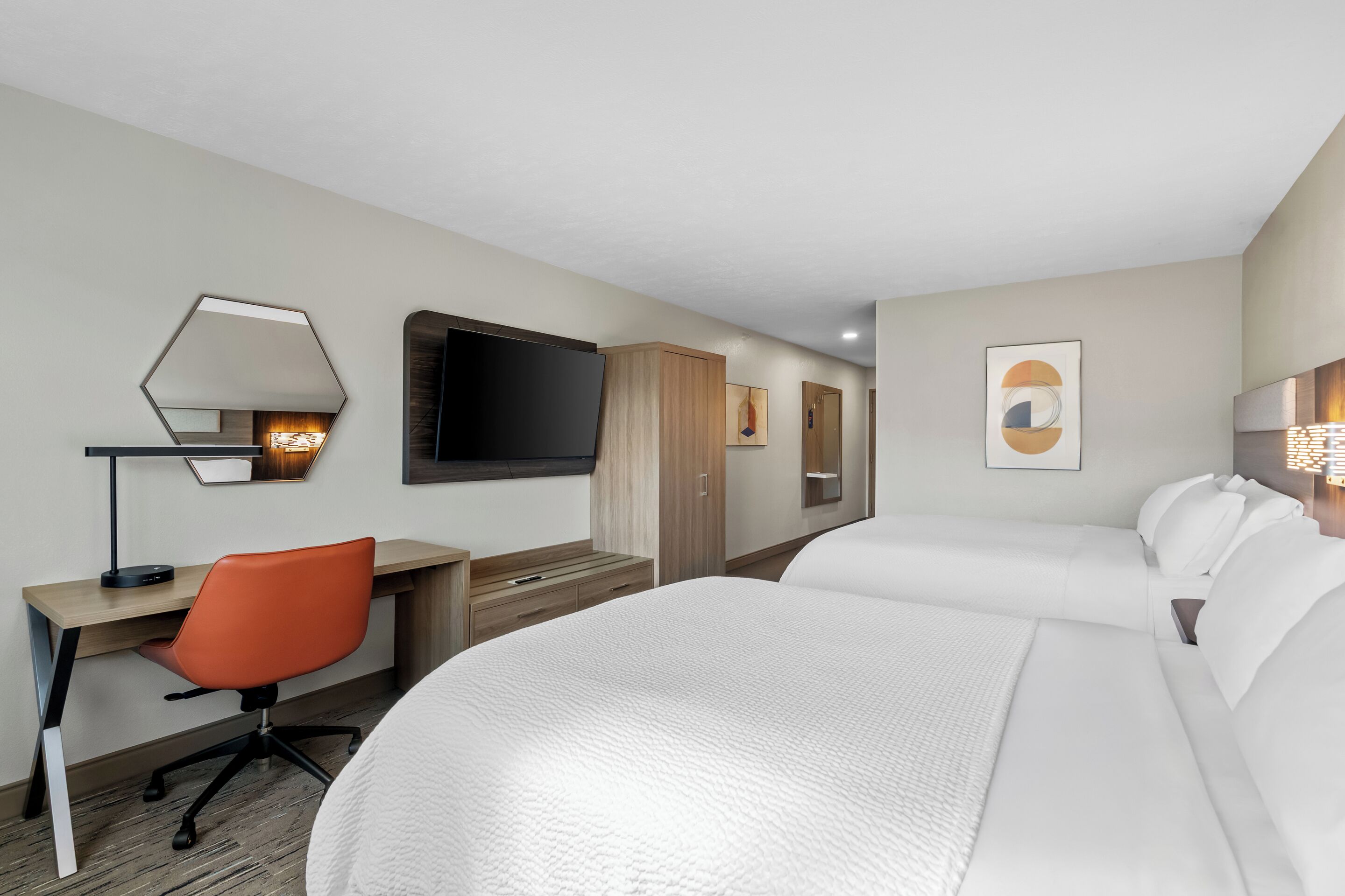 A hotel room with a large bed, a desk with a chair, a TV, and a wardrobe.