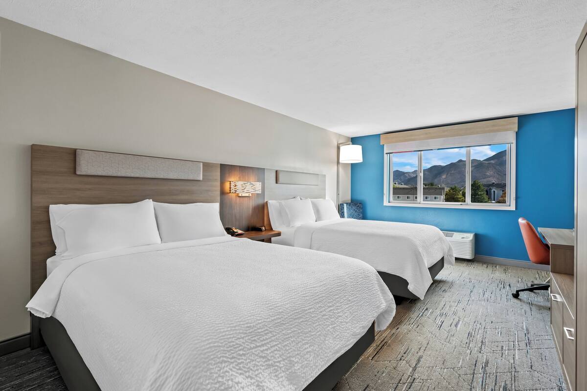 A hotel room with two beds, a desk, and a window with a mountain view.