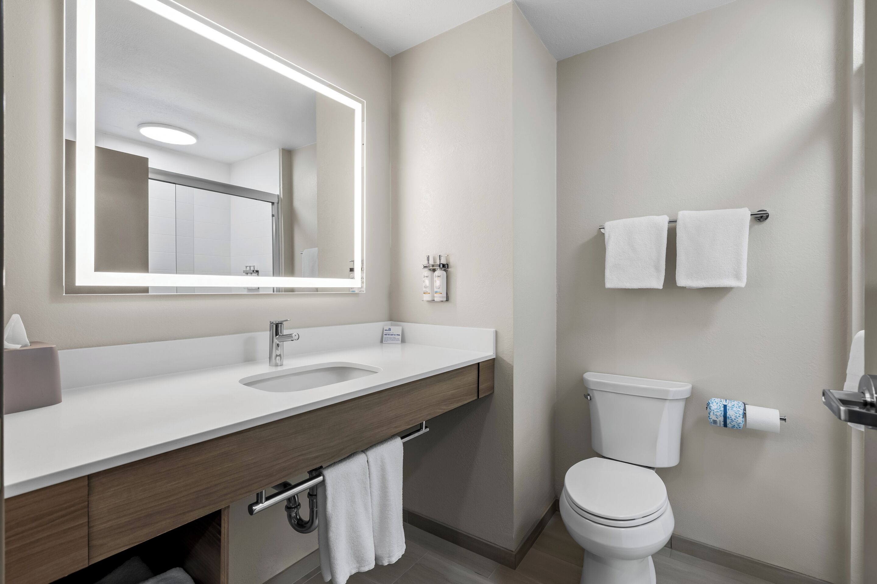 A modern bathroom with a large mirror, a sink, a toilet, and two towels hanging on the wall.