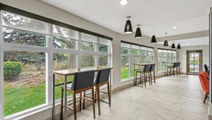Une pièce spacieuse avec de grandes fenêtres, une table en bois et des chaises.