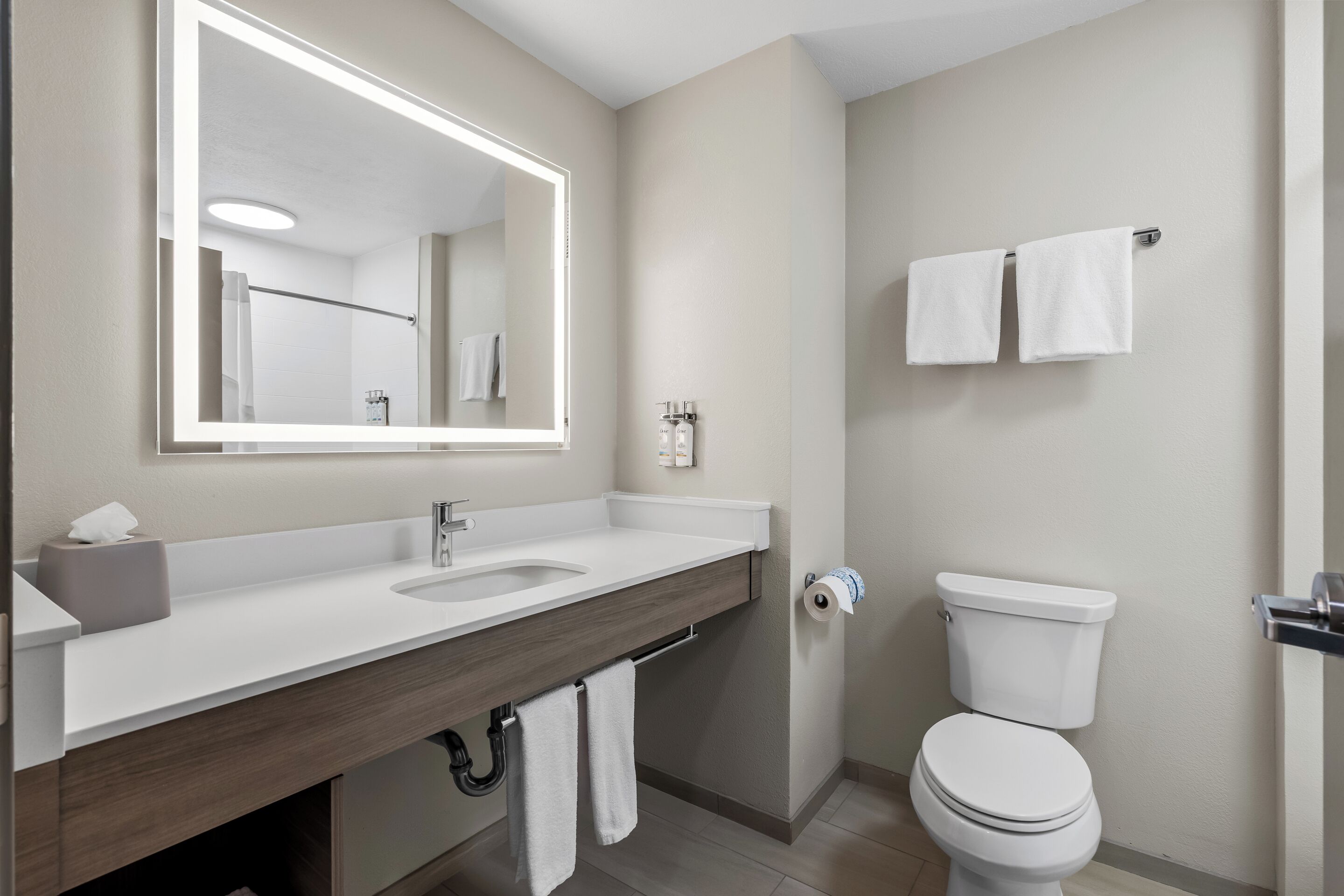 A modern bathroom with a large mirror, a sink, and a toilet.