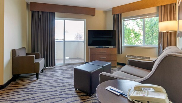 A hotel room with a sofa, armchair, ottoman, flat-screen TV, and a telephone. - Comfort Inn & Suites Market - Airport (Great Falls)