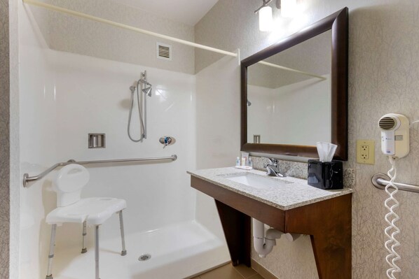 Un baño con una bañera blanca, ducha, tocador con espejo y un secador de pelo en la pared.