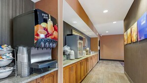 A hotel kitchen with a fruit juice dispenser, stainless steel appliances, and a long counter with various items. - Comfort Inn & Suites Market - Airport (Great Falls)
