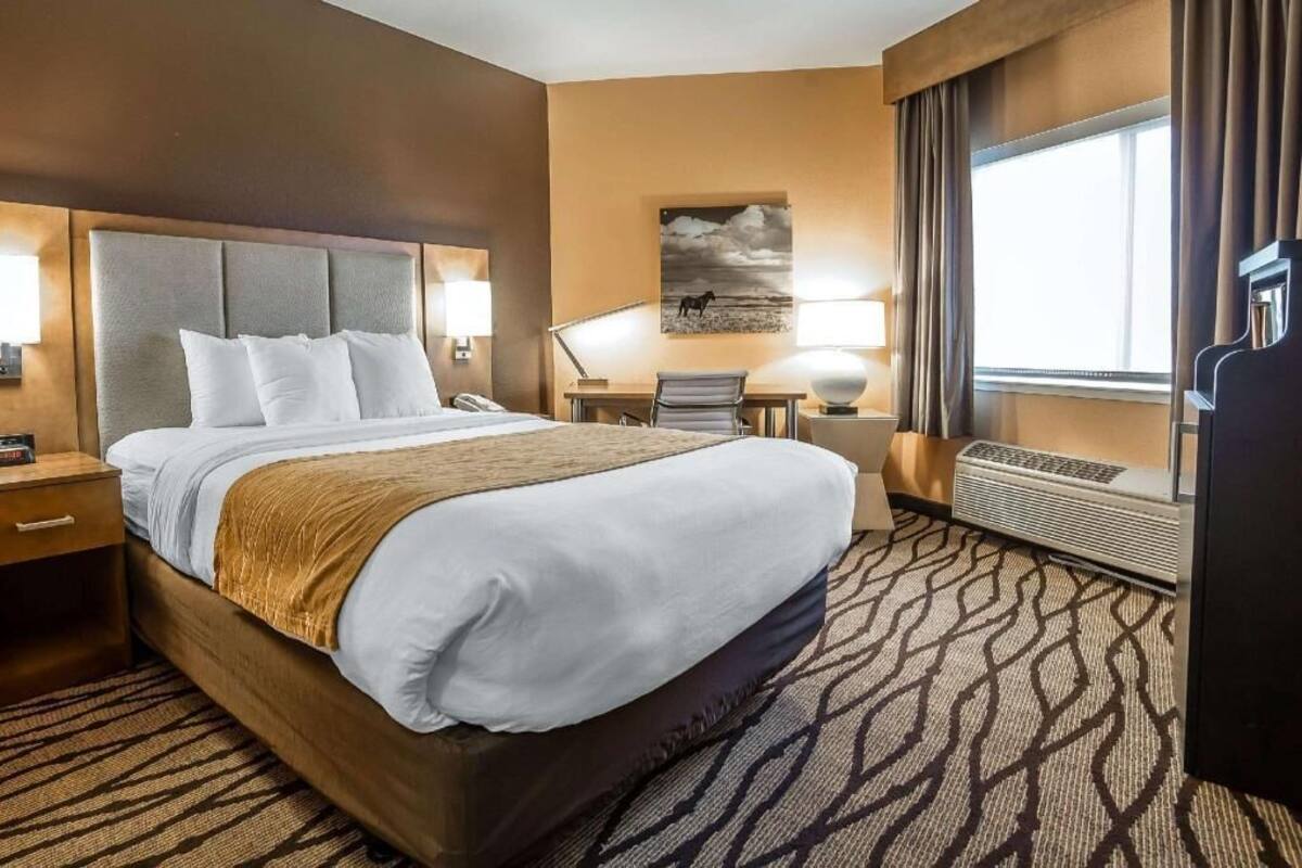 A hotel room with a large bed, bedside tables, a desk, a chair, a lamp, a picture on the wall, and a window with curtains.