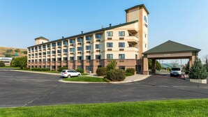 A multi-story hotel with a central entrance, a parking lot, and a small parking garage. - Comfort Inn & Suites Market - Airport (Great Falls)