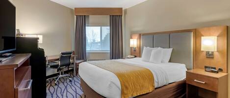 A hotel room with a large bed, a desk with a computer, a TV, and a window with curtains.