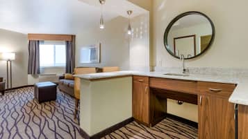 Una habitación de hotel con kitchenette, un espejo grande, un sofá y una alfombra estampada.