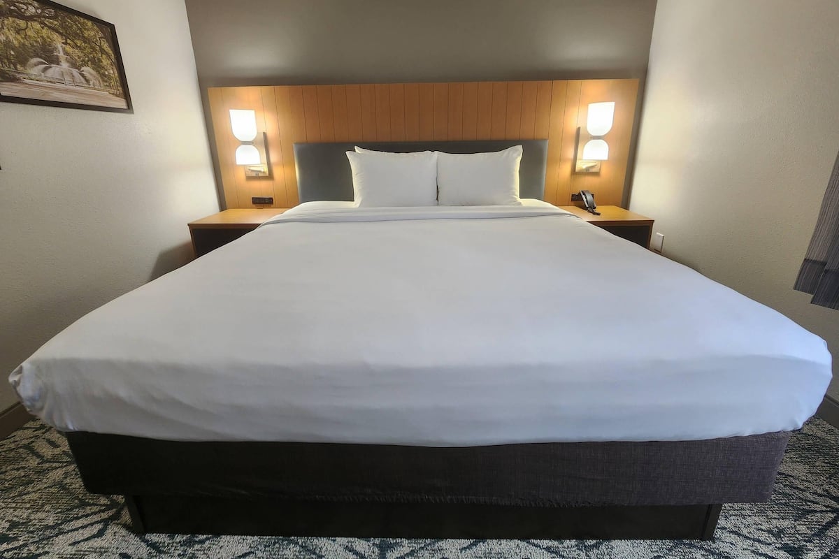 A hotel room with a large bed, two bedside lamps, a wooden headboard, and a framed picture on the wall.
