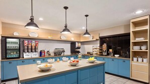 A modern kitchen with blue cabinets, a central island with bowls of food, and overhead pendant lighting. - Country Inn & Suites by Radisson, Dahlgren-King George, VA (King George)