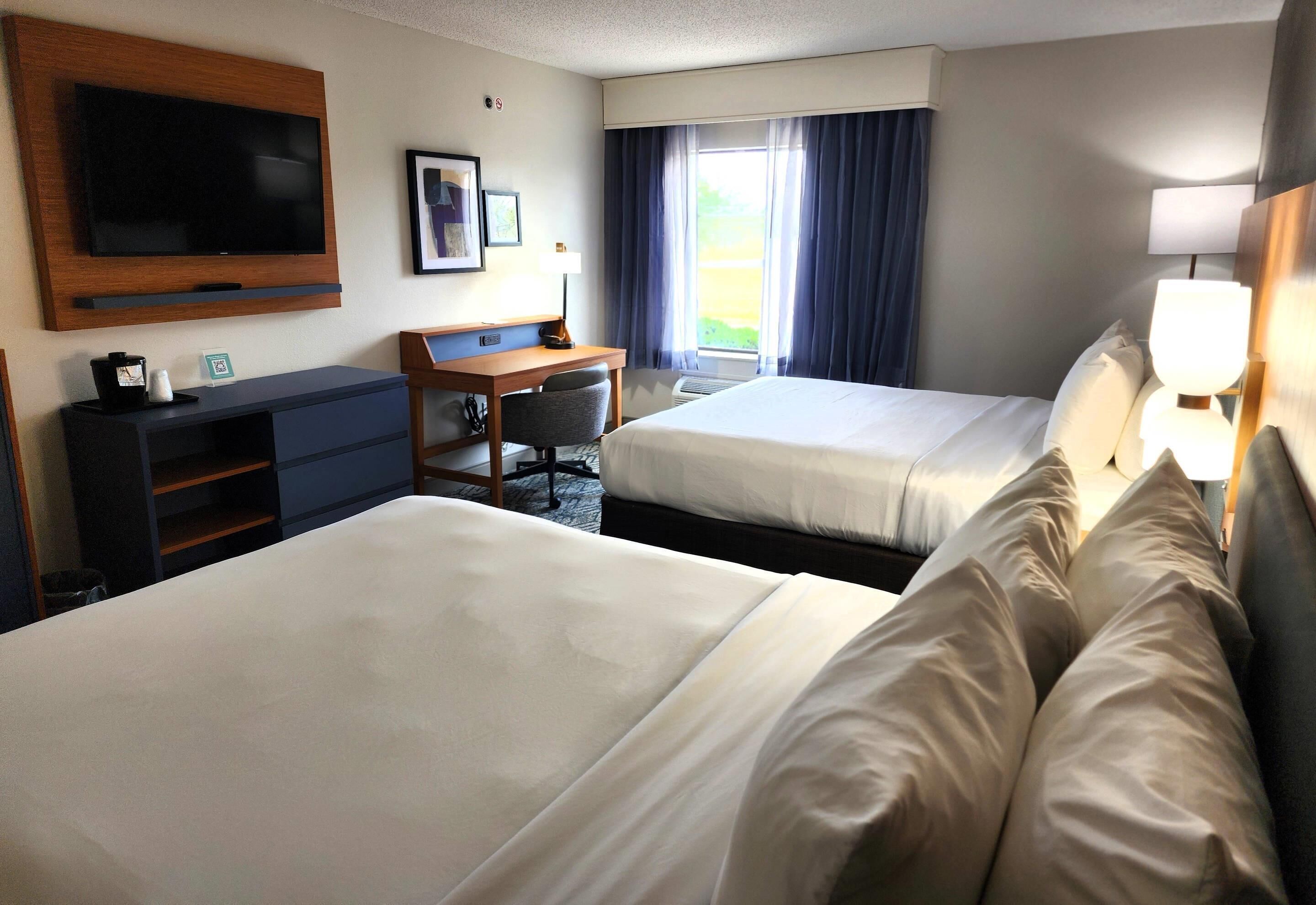Une chambre d’hôtel avec deux lits, un bureau, une télévision et une fenêtre avec des rideaux.