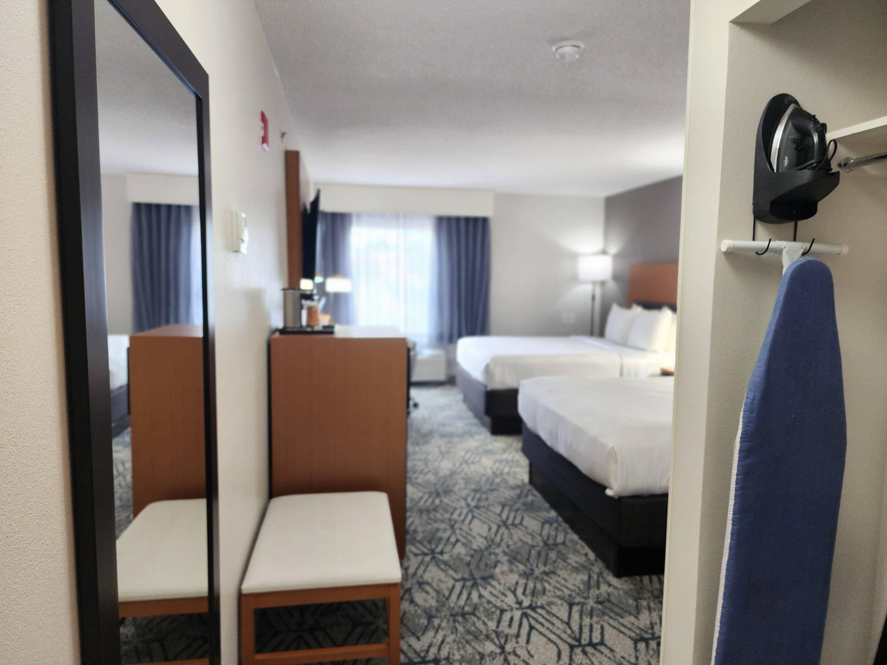 A hotel room with two beds, a desk, a chair, a mirror, and a blue towel rack.