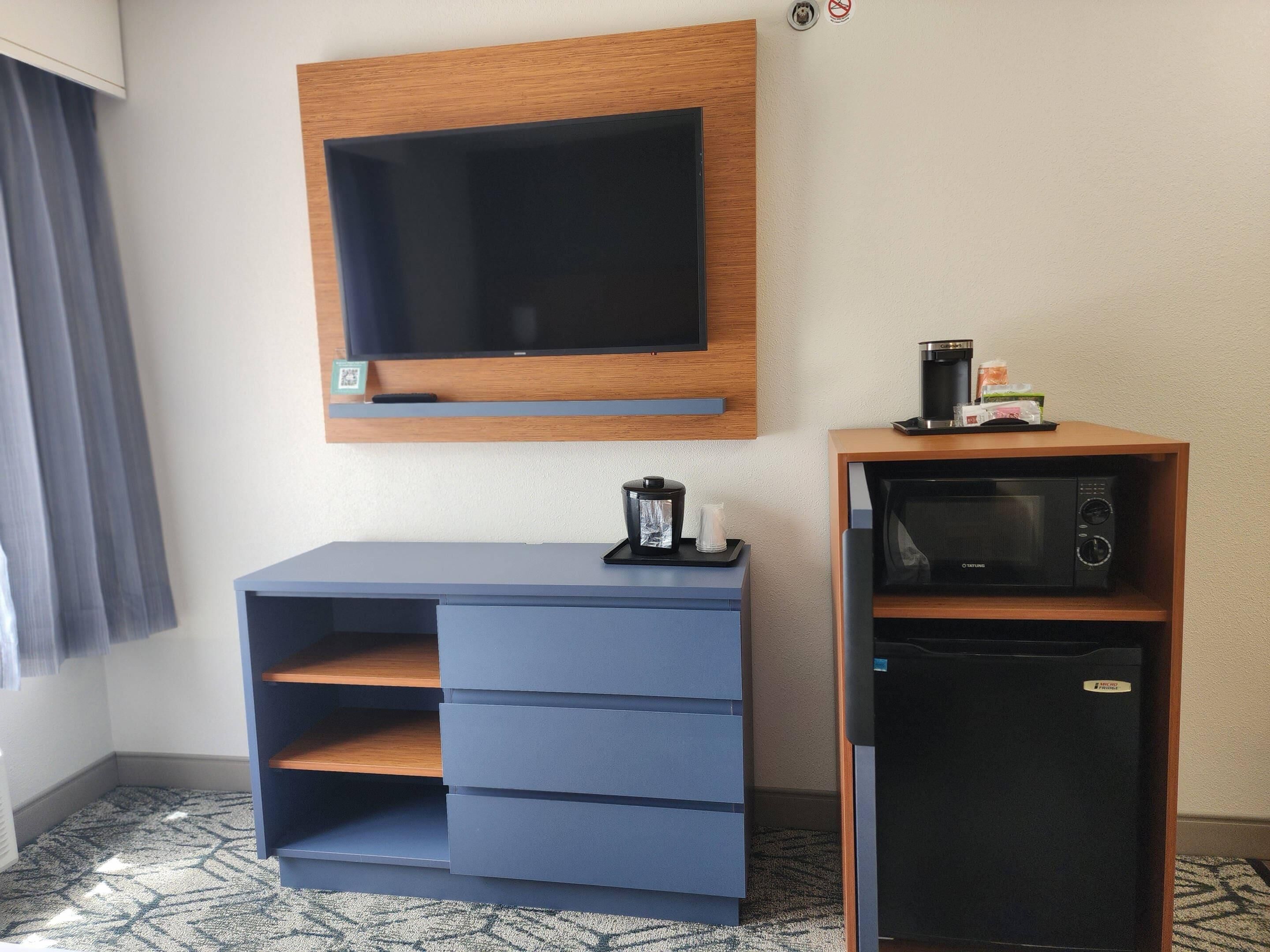 Camera d'albergo con TV a schermo piatto fissata al muro, macchina del caffè e forno a microonde su un mobile in legno.