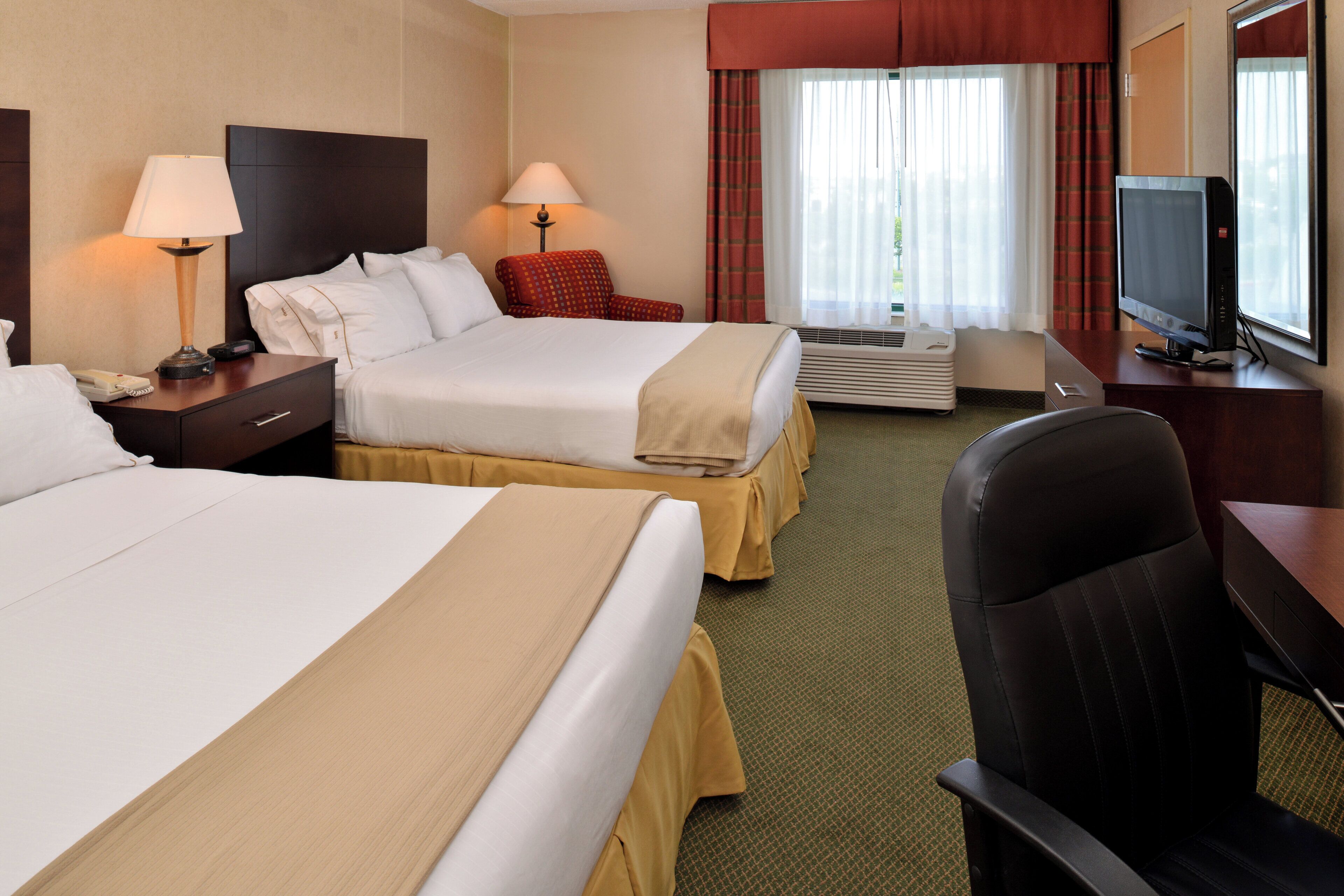 A hotel room with two beds, a desk, a television, and a window with curtains.