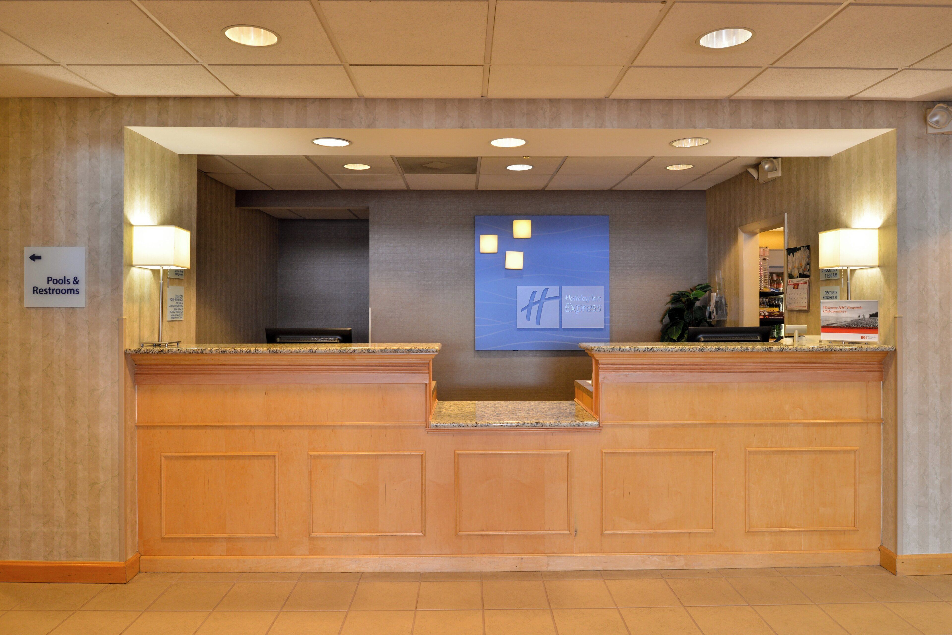 A hotel reception desk with a sign for pools and restrooms, a blue wall with a logo, and a counter with a lamp.