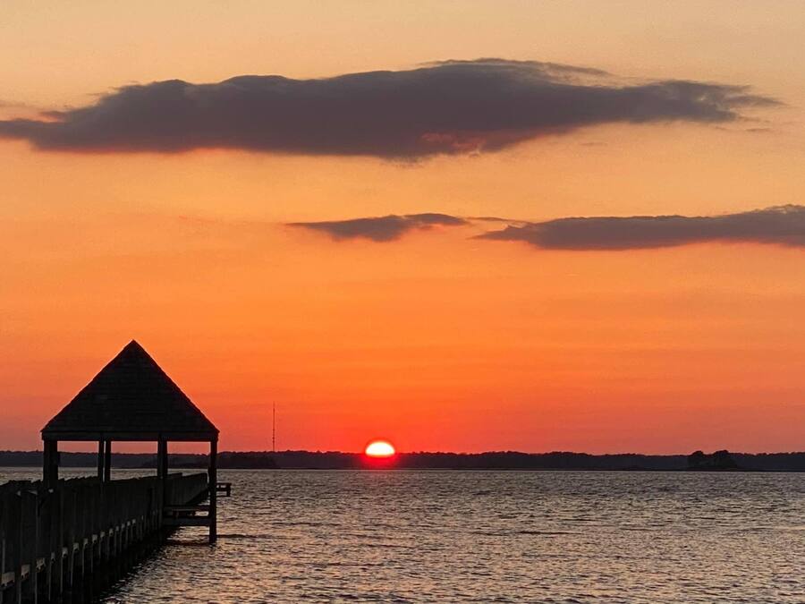 Ein Sonnenuntergang über einem Gewässer mit einem hölzernen Steg und einem Pavillon.