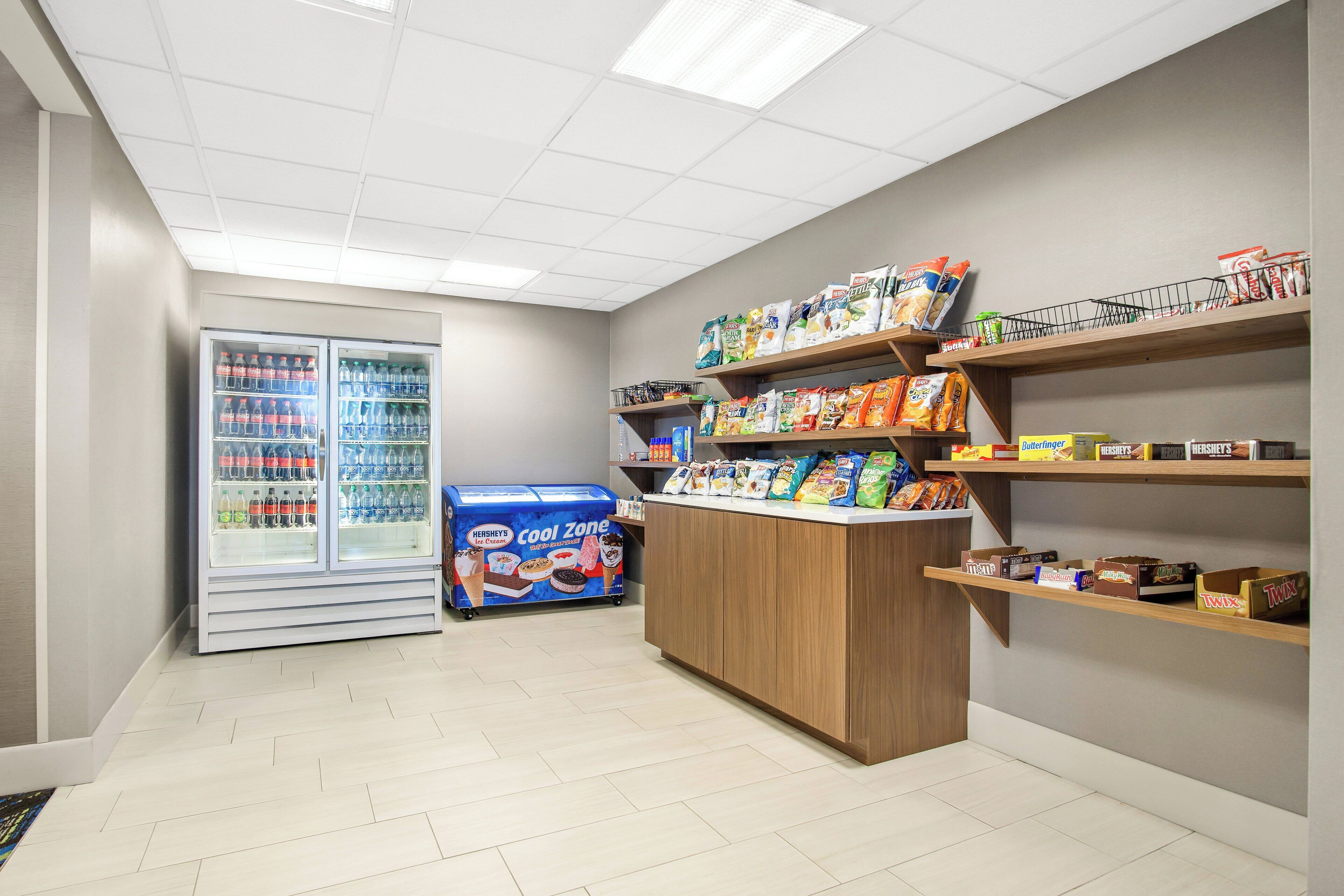 Een snackgedeelte met een koelvitrine, een Hershey's Cool Zone ijskoeler en planken vol met verschillende snacks en verpakte waren.
