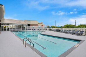 A swimming pool with lounge chairs and umbrellas, surrounded by a white fence and a building with a glass facade. - Holiday Inn Express Hotel & Suites Ocean City by IHG (Ocean City)