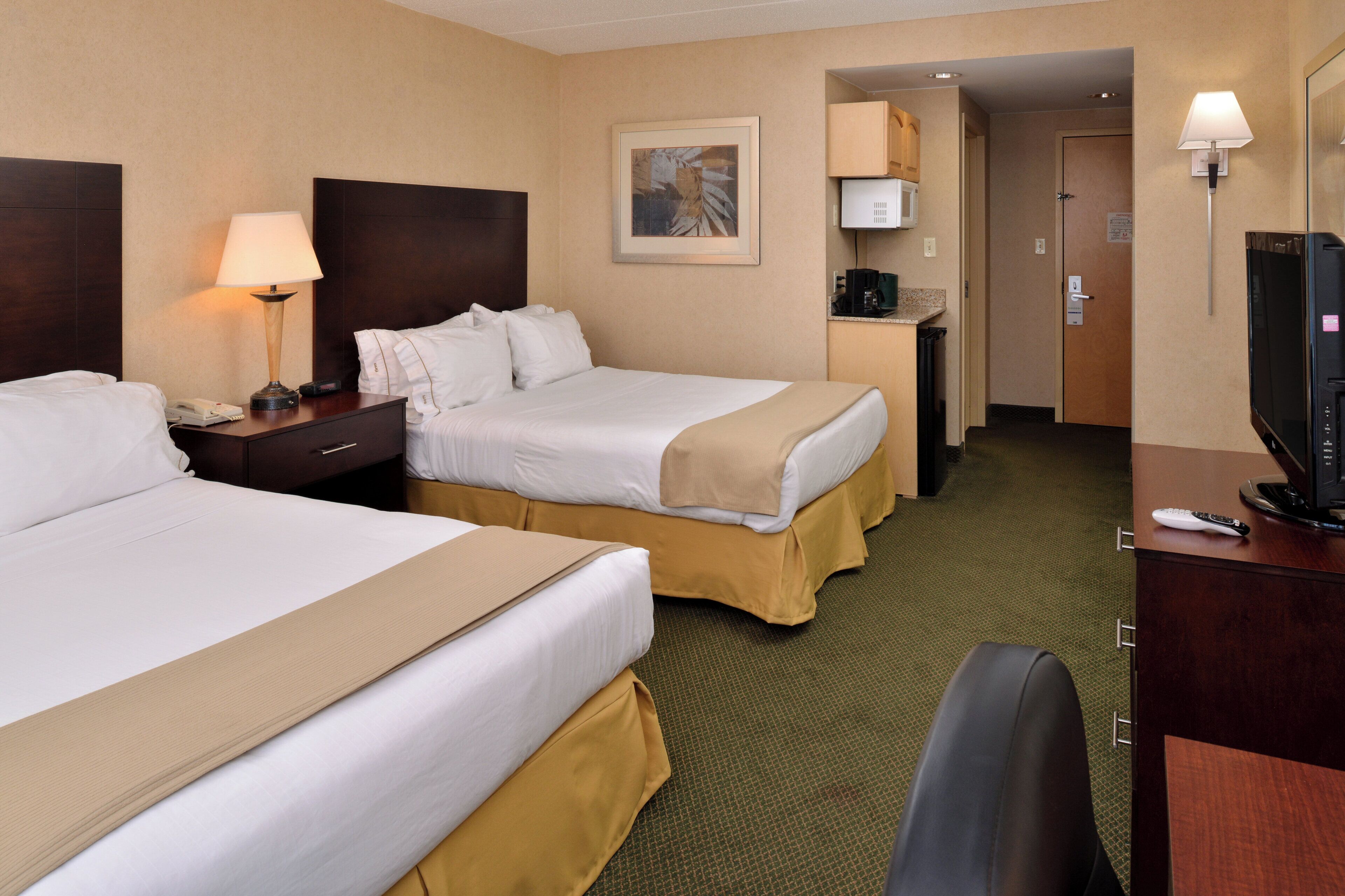 A hotel room with two beds, a desk, a chair, a television, and a coffee machine.