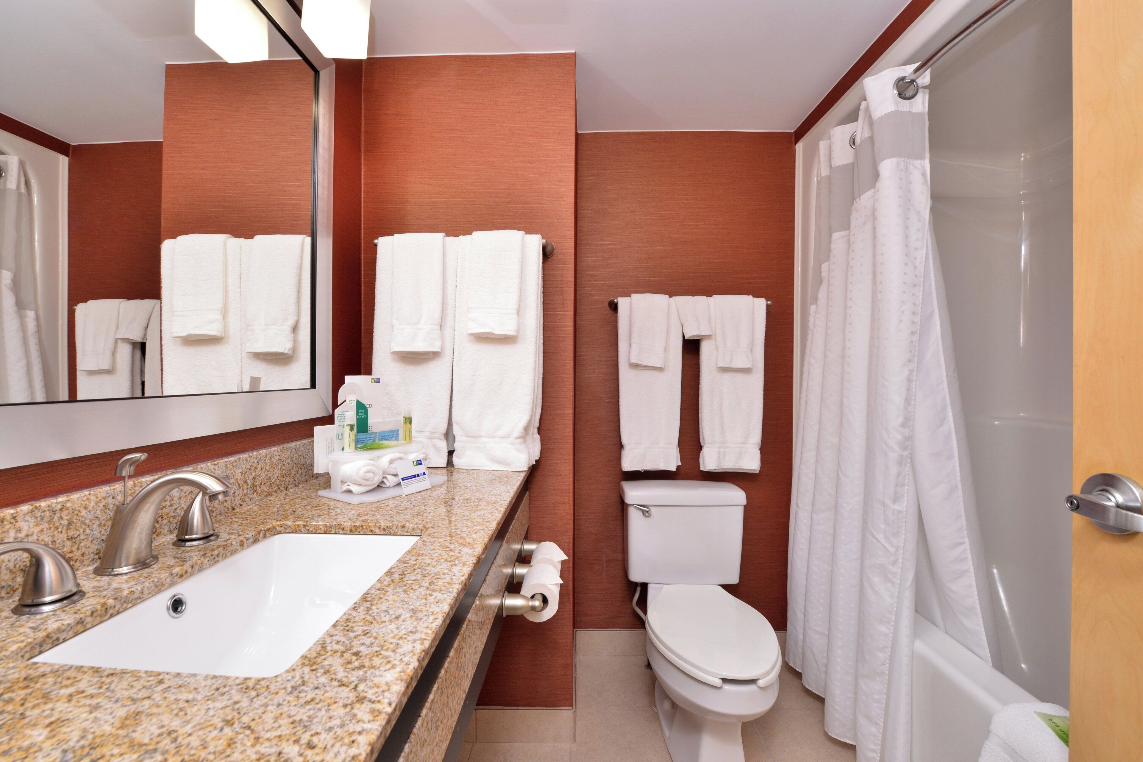 A bathroom with a granite countertop, a sink, a toilet, and a shower with a curtain.