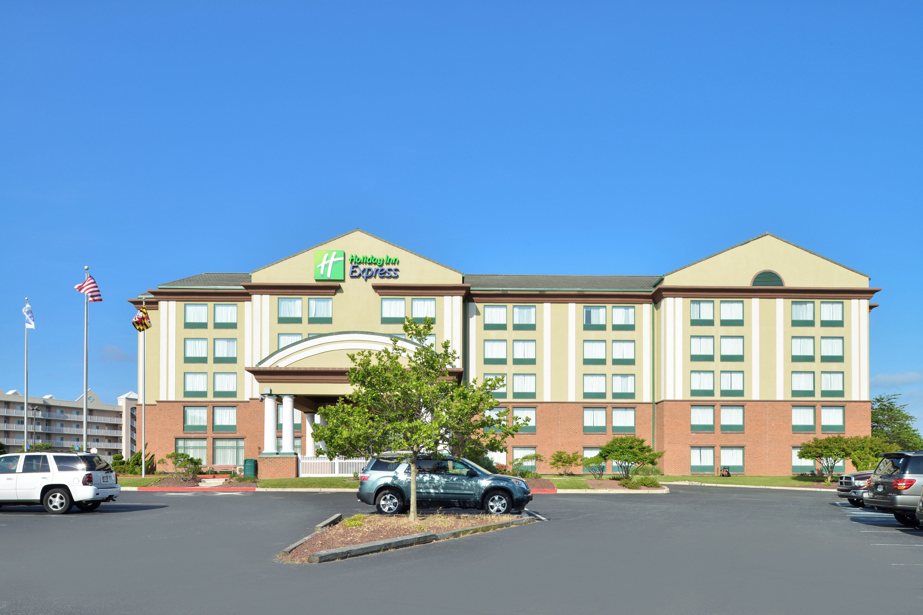 Edificio de Holiday Inn Express con entrada central, varias ventanas y aparcamiento con coches.