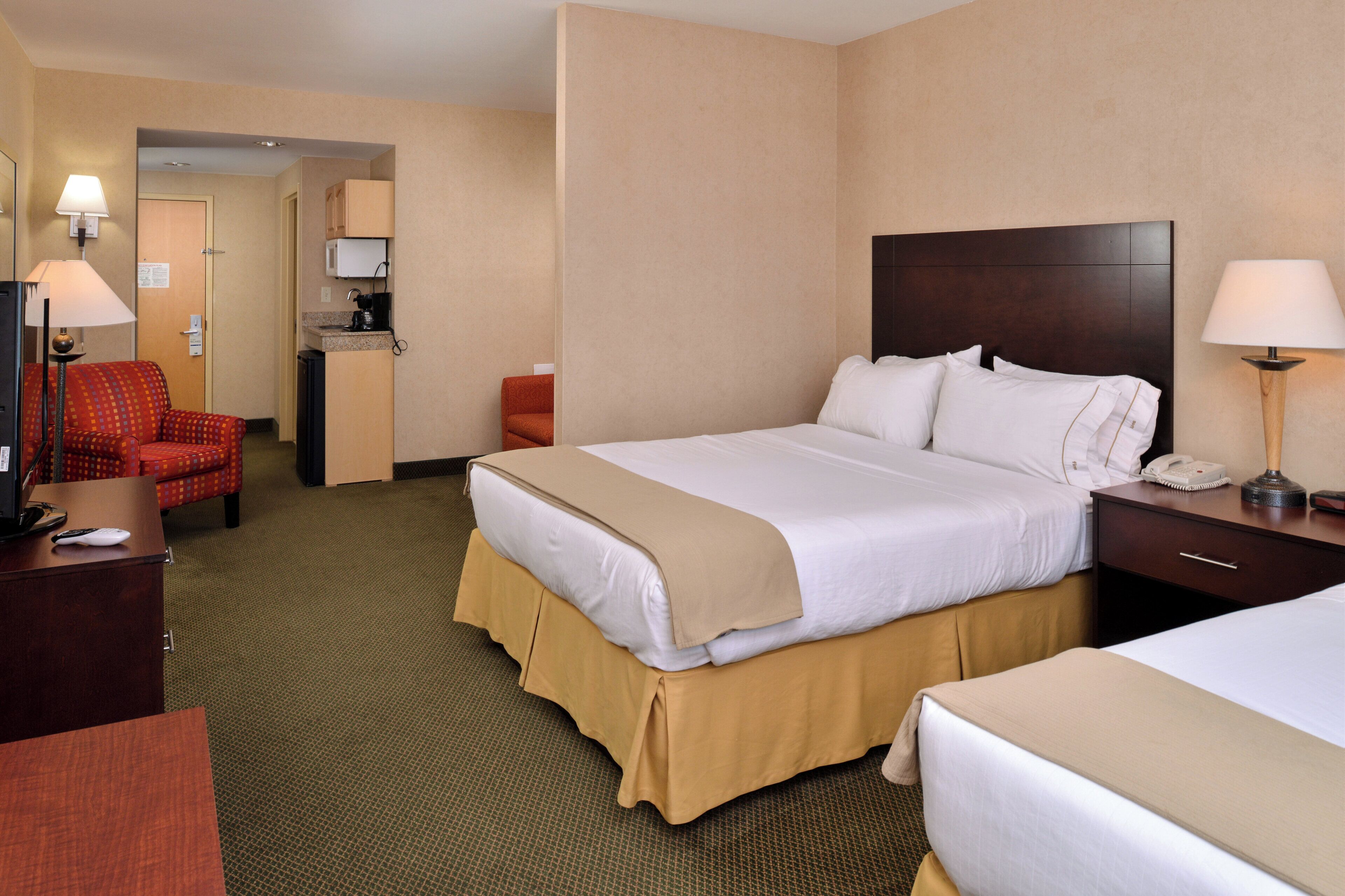 A hotel room with a bed, bedside tables, a desk, a chair, and a kitchenette area.