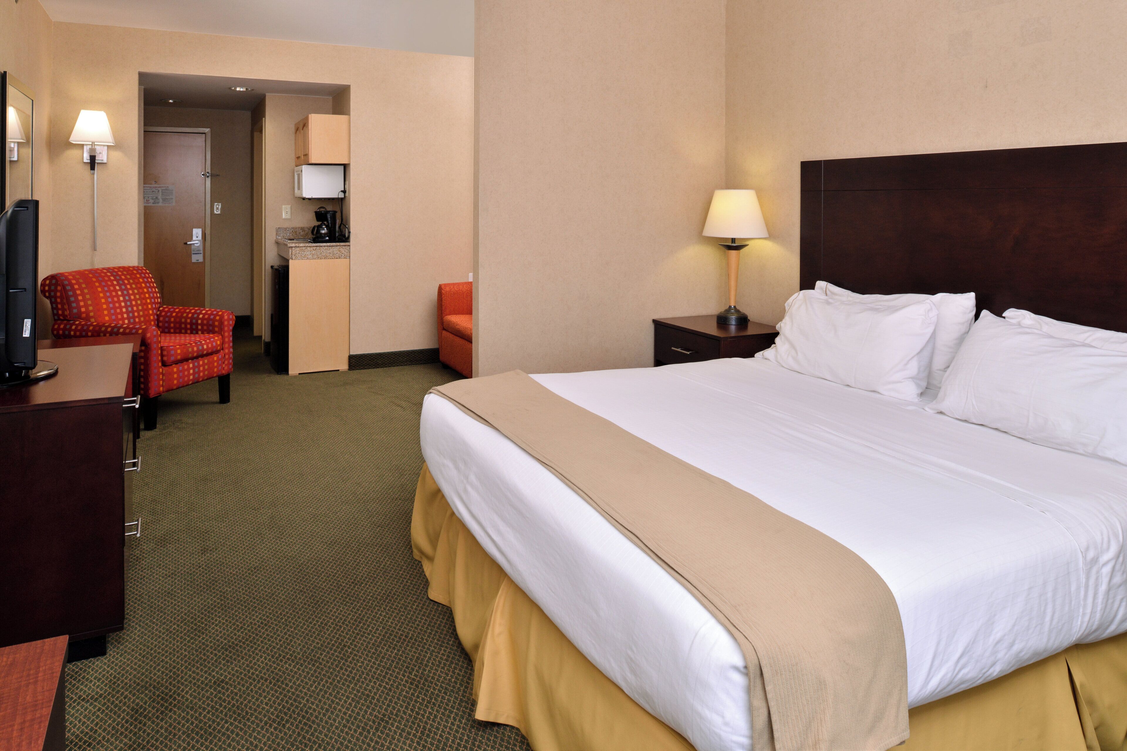 A hotel room with a bed, a desk, a television, a chair, a nightstand, and a lamp.